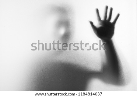 Shadow blur of horror man in fancy mask.Hands on the glass.Dangerous man behind the frosted glass.Mystery man.Halloween background.Black and white picture.Blur picture.