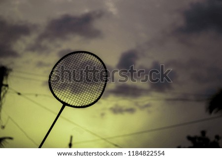 A silhouette badminton and tennis bat raised up in air with a cloudy dark sky