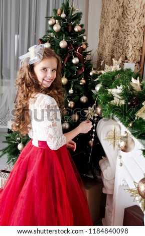 Adorable happy smiling little girl child in princess dress with gift box near fir tree in christmas time