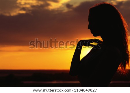 silhouette of a beautiful dreamy girl at sunset in a field, face profile of young woman on nature