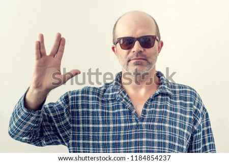 Portrait of an adult man with a gray beard, dark glasses shirt showing a gesture Star Trek, planet Vulcan