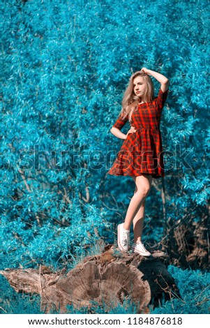Textile, design, clothing, fashion concept. teenager showing clothes. Beautiful young woman in a beautiful dress on a background of blue foliage. Standing on the stump