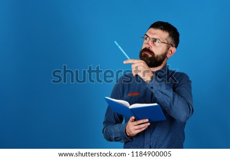 Notebook in blue color in guys hands on blue background. Professor with concentrated face. Man with beard, book and marker. Knowledge and lesson concept. Teacher wears glasses and holds organizer