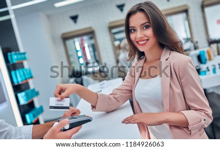 Attractive young woman is spending time in beauty salon. Paying via credit card.
