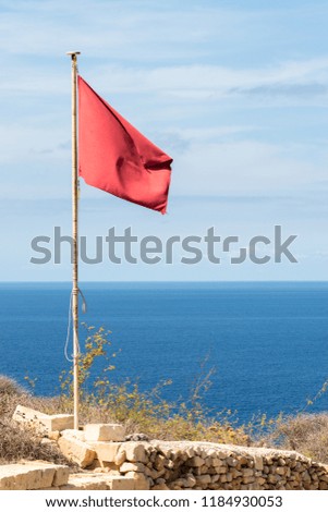 Red flag waving on a pole. Clouds and sea view background. Vertical 