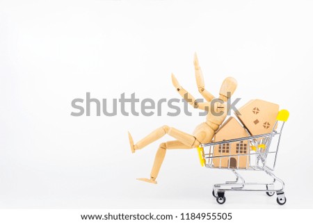 Wooden human mannequin holding shopping cart full of paper hose model, isolated on white background with copy space.Real estate concept, New house concept.Buying a house