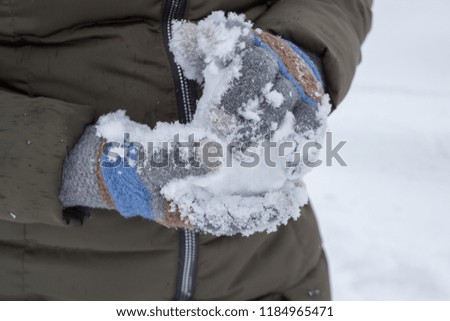 a sculpts a snowball,a woman wearing gloves takes snow