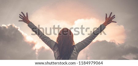 Woman backs on top of the mountain raises her hands to the sky as a sign of rejoicing