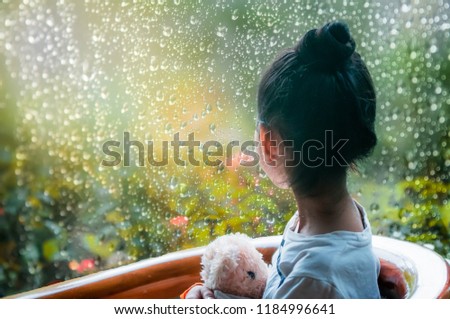 A little girl sitting in front of a mirror with a droplet of rain in the morning.