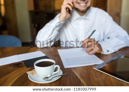 businessman is talking on the phone, drinking coffee and signing