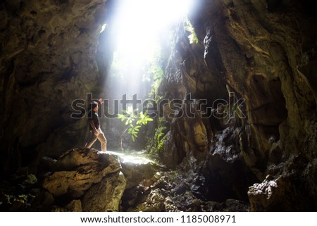 Backside of Asian man traveler stand under the ray of light in the cave. Form Thailand. Travel concept.