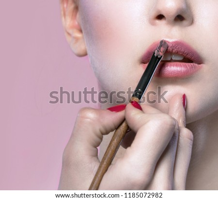 portrait of attractive caucasian young woman brunette on pink background studio shot face hand makeup artist applying lipstick lips