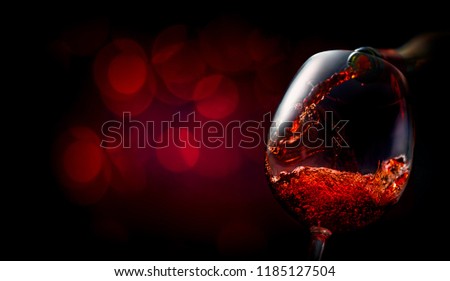 Wine pouring into wineglass on dark red background