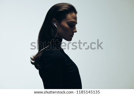Silhouette of female model in studio. Side view of young woman wearing earphones on grey background.