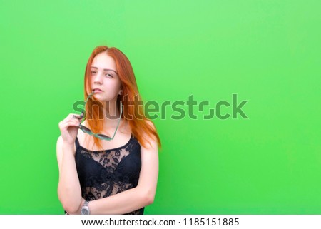 Cheerful red hair woman posing in trendy black blouse. Female with long red hair and engaging appearance looking front. Isolated on green. Copy space in right side