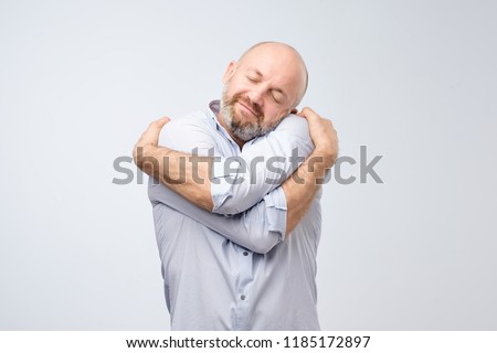 Closeup portrait of confident smiling man holding hugging himself isolated on grey wall background. Positive human emotion, facial expression. Love yourself concept Royalty-Free Stock Photo #1185172897