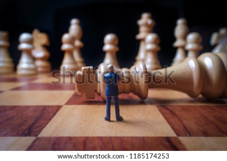 Miniature businessmen battle with giant chesspieces for symbolic metaphor Royalty-Free Stock Photo #1185174253