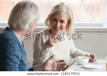 Smiling beautiful middle aged mature woman drinking coffee tea listening to older man talking during breakfast, senior happy family couple eating having pleasant conversation on date at home in café Royalty-Free Stock Photo #1185179011