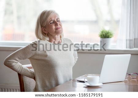 Upset mature middle aged woman feels back pain massaging aching muscles, sad senior older lady suffers from low-back lumbar pain sitting in incorrect sedentary posture, backache radiculitis concept Royalty-Free Stock Photo #1185179191