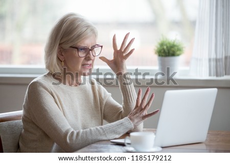 Angry stressed senior middle aged business woman annoyed with computer problem, old office worker hates stuck laptop, mad mature lady frustrated about bad online news, data loss, software failure Royalty-Free Stock Photo #1185179212