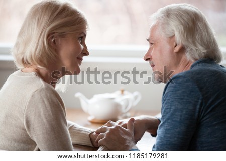 Happy loving senior middle aged retired family couple holding hands looking in the eyes giving care psychological support to older, understanding in good relations, trust devotion in marriage concept Royalty-Free Stock Photo #1185179281