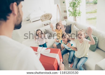 Who wants a gift? Me! Funky, funny, positivity, rejoice, laugh concept. High angle above top view dad hold prize for kids, who sit on soft couch in modern light interior