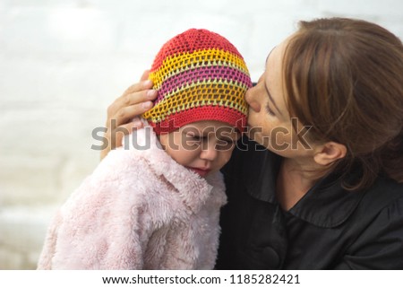 Caucasian middle aged woman kissing with tenderness crying with tears two years old child on white brick background