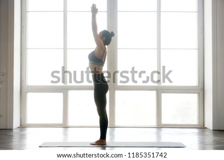 Young sporty attractive woman practicing yoga, doing mountain exercise, Tadasana pose, working out, wearing sportswear, grey pants, top, indoor full length, at white at yoga studio, side view