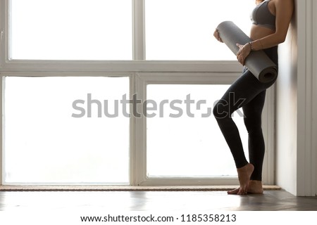 Close up legs, young slim woman holding yoga fitness mat before doing yoga, female instructor after work out at home or club, standing near window. Healthy lifestyle, hobby, beauty, well being concept Royalty-Free Stock Photo #1185358213