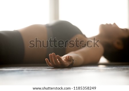 Young sporty attractive woman practicing yoga, doing Dead Body exercise, Savasana, Corpse pose, working out, wearing sportswear, grey top, indoor close up, at yoga studio, focus on fingers Royalty-Free Stock Photo #1185358249