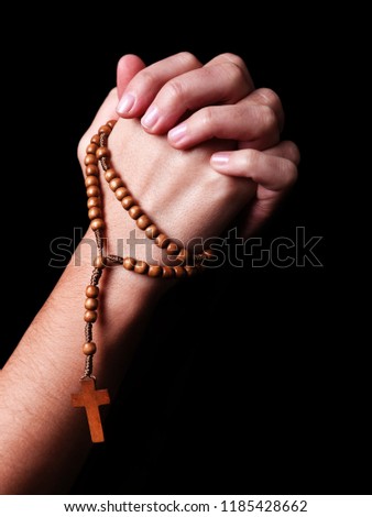 Female hands praying holding a beads rosary with a cross or Crucifix on black background. Woman with Christian Catholic religious faith. Profile or side view
