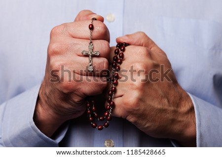 Male hands praying holding a beads rosary with Jesus Christ in the cross or Crucifix on black background. Mature man with Christian Catholic religious faith Royalty-Free Stock Photo #1185428665