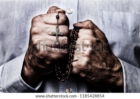 African American male hands praying holding a beads rosary with Jesus Christ in the cross or Crucifix on black background. Mature Afro American man with Christian Catholic religious faith Royalty-Free Stock Photo #1185428854