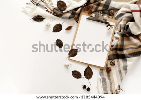 Autumn background composition with mock up clipboard, scarf in a cage and autumn leaves on a white background. Flat lay. Top view. Copy space