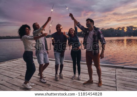 Creating happy memories. Full length of young people in casual wear smiling and holding sparkers while standing on the pier Royalty-Free Stock Photo #1185454828