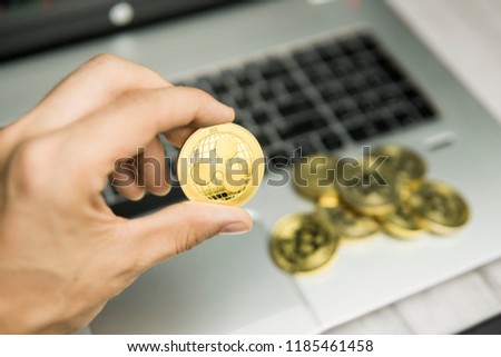 Male businessman hand holding Ripple coin on a background of laptop keyboard and pile of golden coins. Virtual money and Financial growth concept. Trading Mining of Ripples.