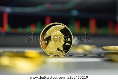 Golden titan bitcoin coin with gold coins lying around on a silver keyboard of laptop and diagram chart graph on a screen as a background. Mining of bitcoins online bussiness. Titans trading.