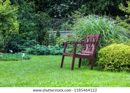 Beautiful landscape design of the house territory. A bench on a green lawn with flowering ornamental plants