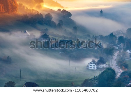 Scenic foggy mountain landscape at sunset. View on a picturesque village in Germany, Black Forest. Colorful travel background.