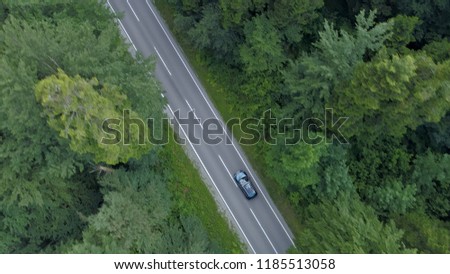 AERIAL, TOP DOWN: Flying above a car cruising through the beautiful dark green forest. Cinematic shot of dark colored car on a scenic journey down empty asphalt road running through the countryside.