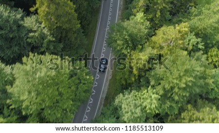 AERIAL, TOP DOWN: Dark car drives along an empty forest road in sunny Slovenia. Car speeds down an asphalt trail leading through the idyllic countryside. Cinematic shot of car driving through woods.
