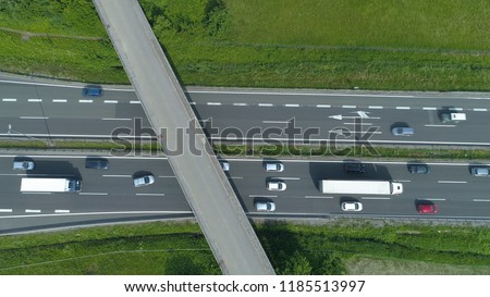 AERIAL, TOP DOWN: Colorful vehicles move along the busy freeway and under a concrete overpass. Flying above cars and trucks driving up and down a bustling highway running through the green nature.