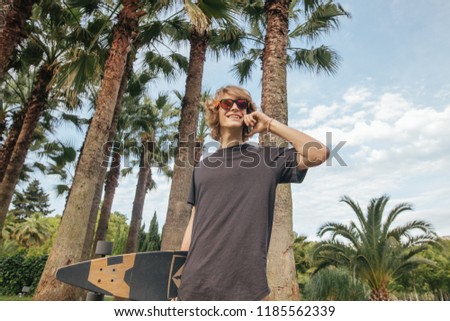 handsome young skateboarder walking with longboard in hand and talking phone