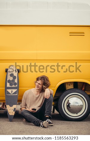 Young man using a cellphone while sitting at longboard
