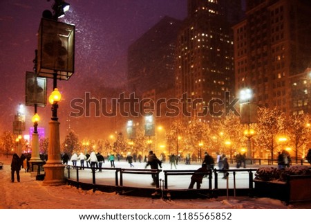 Winter snowy night in a city. Background with silhouettes of people enjoying ice skating during beautiful snowy winter night in downtown of Chicago in shallow depth of field.