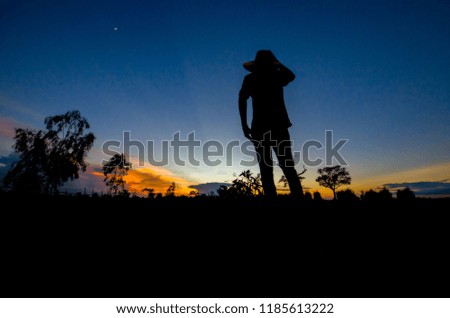 Thai farmer are watching sunset at dusk on rice field. Background is beautiful blue sky and cloud. Picture is silhouette style.