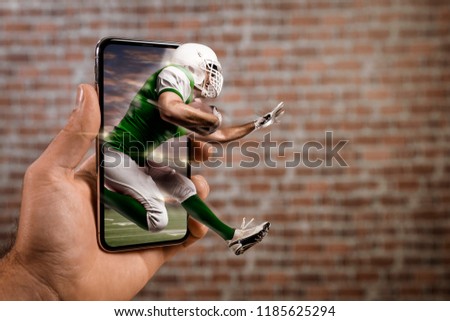 Football Player with a green uniform playing and coming out of a full screen phone in front of a brick wall. Watching a football game on demand concept. copy space.