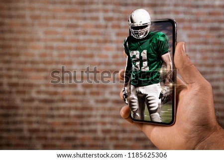 Football Player with a green uniform playing and coming out of a full screen phone in front of a brick wall. Watching a football game on demand concept. copy space.