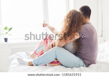 Lovely girlfriend and boyfriend dressed casually, enjoy intimacy and togetherness, pose on bed in bedroom, look at window, have pleasant talk, express good feeling to each other. Bed time concept