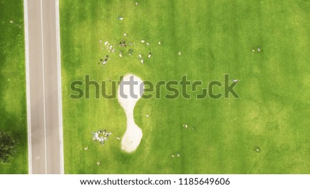 Aerial or overhead view of people enjoying picnics in a large grass field next to a lake surrounded by trees on a lovely sunny day